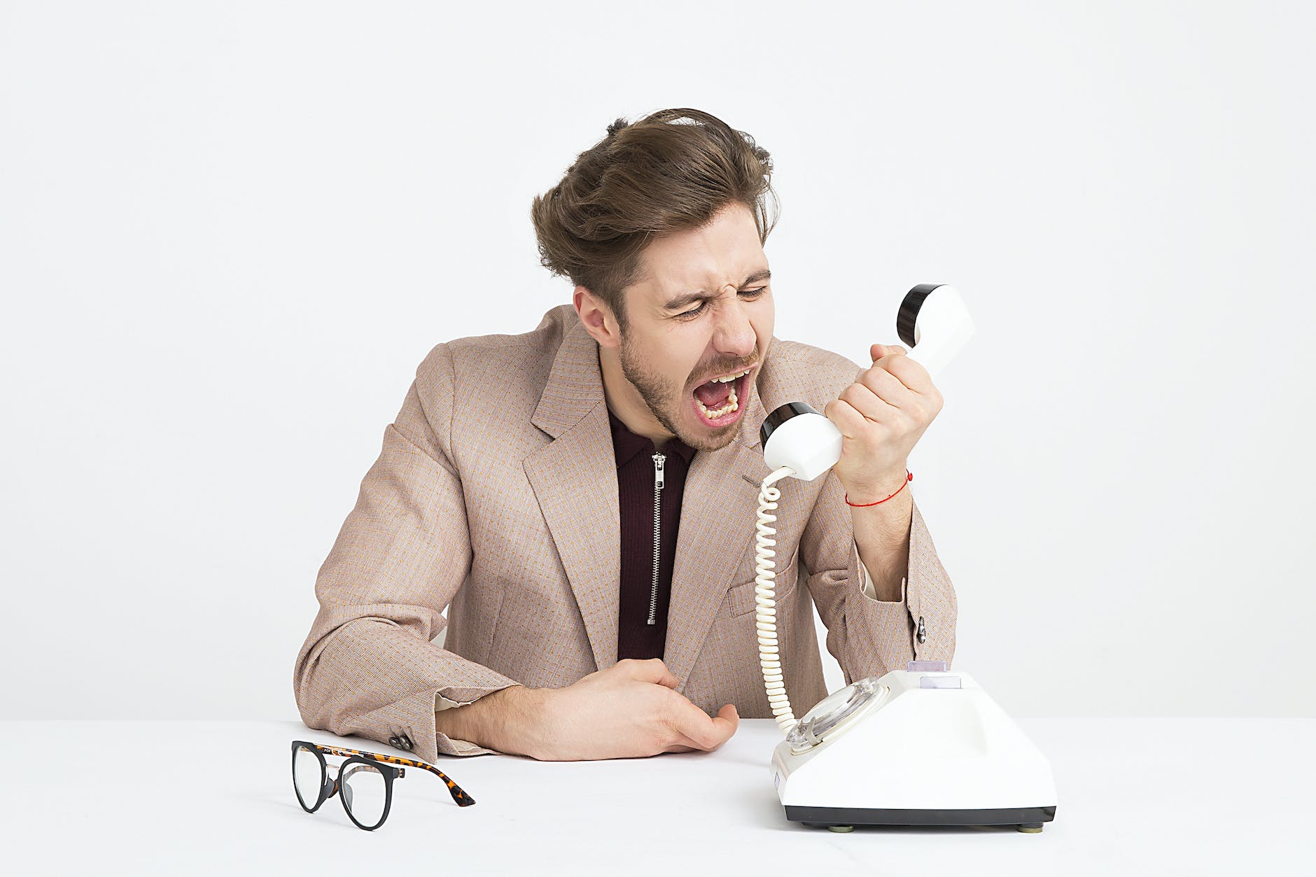 man wearing brown suit jacket mocking on white telephone