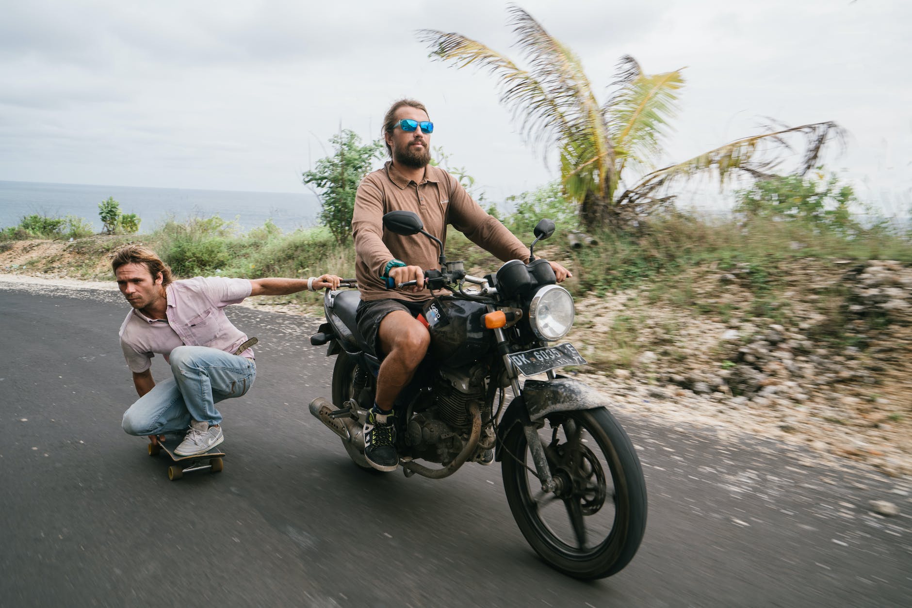 biker riding motorcycle and pulling skater without helmet